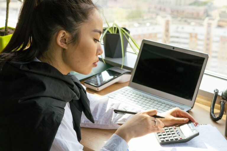 Professionnelle de la comptabilite utilisant un ordinateur portable et une calculatrice au bureau, illustrant l'apport de l'intelligence artificielle